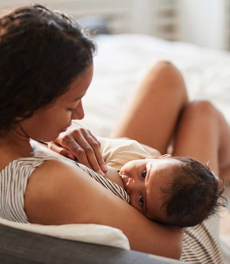 A woman breastfeeds her child in a cozy bedroom