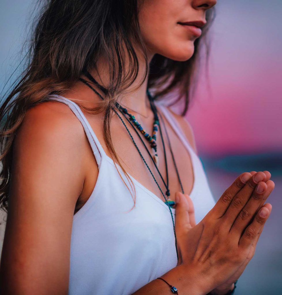 a woman on a beach holds her hands together in a peaceful praying gesture