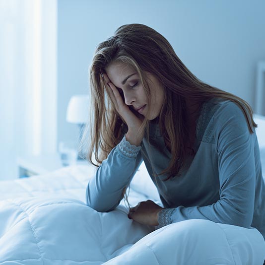 An exhausted looking woman in pajamas sits up in bed