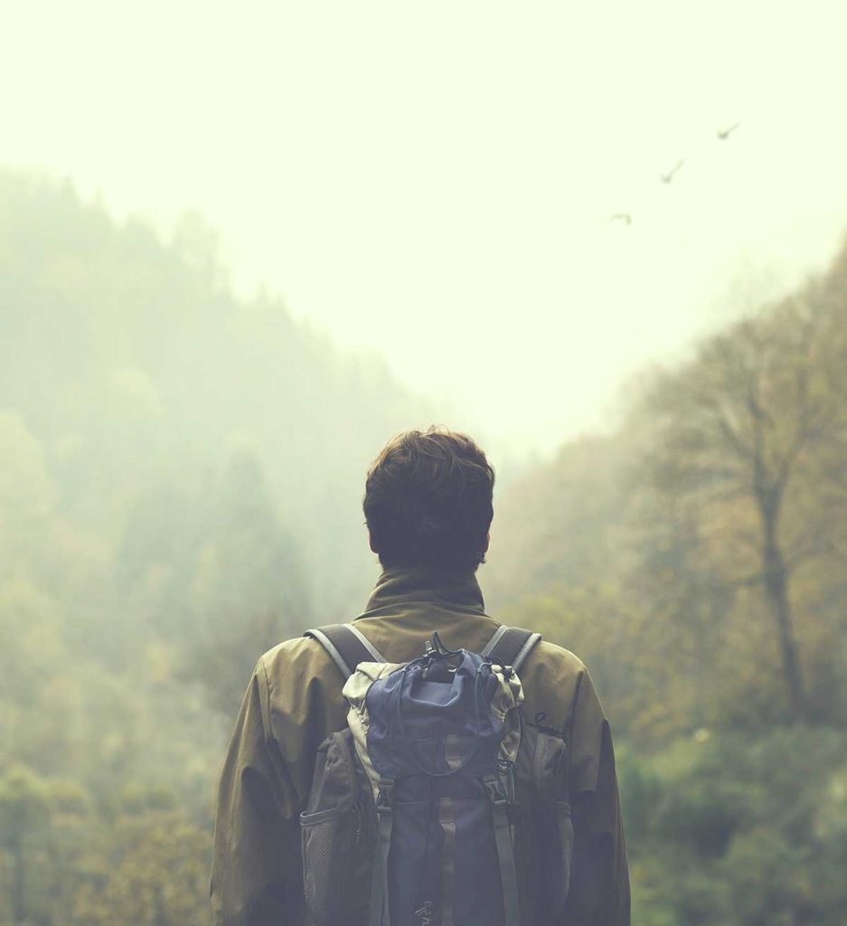 a hiker stands in front of a misty mountain wistfully